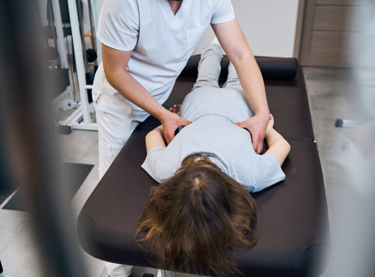 Terapeuta wykonujący masaż pleców na stole do terapii z pacjentem w szarym stroju.