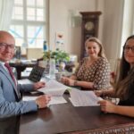 Trzy osoby siedzące przy stole, przeglądające dokumenty w biurze.