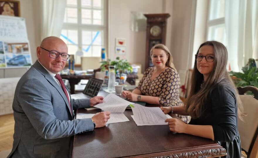 Trzy osoby siedzące przy stole, przeglądające dokumenty w biurze.