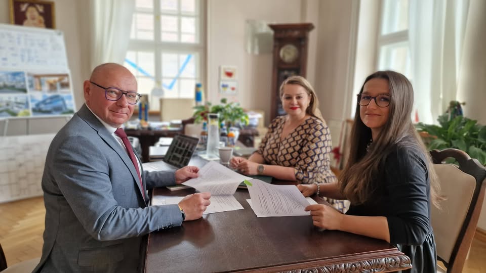 Trzy osoby siedzące przy stole, przeglądające dokumenty w biurze.